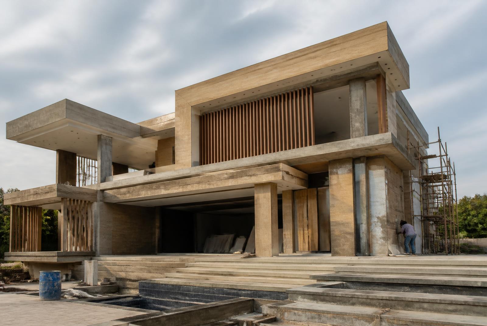 Contemporary Indian luxury residence at an advanced construction stage with precise concrete geometry and warm timber screens