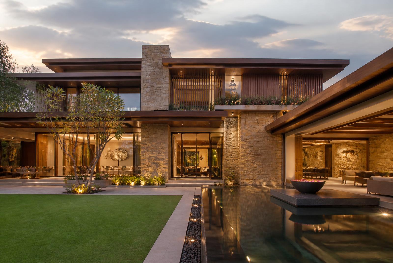 Completed modern Indian luxury residence in stone and warm wood with refined landscaping and a still water court at dusk